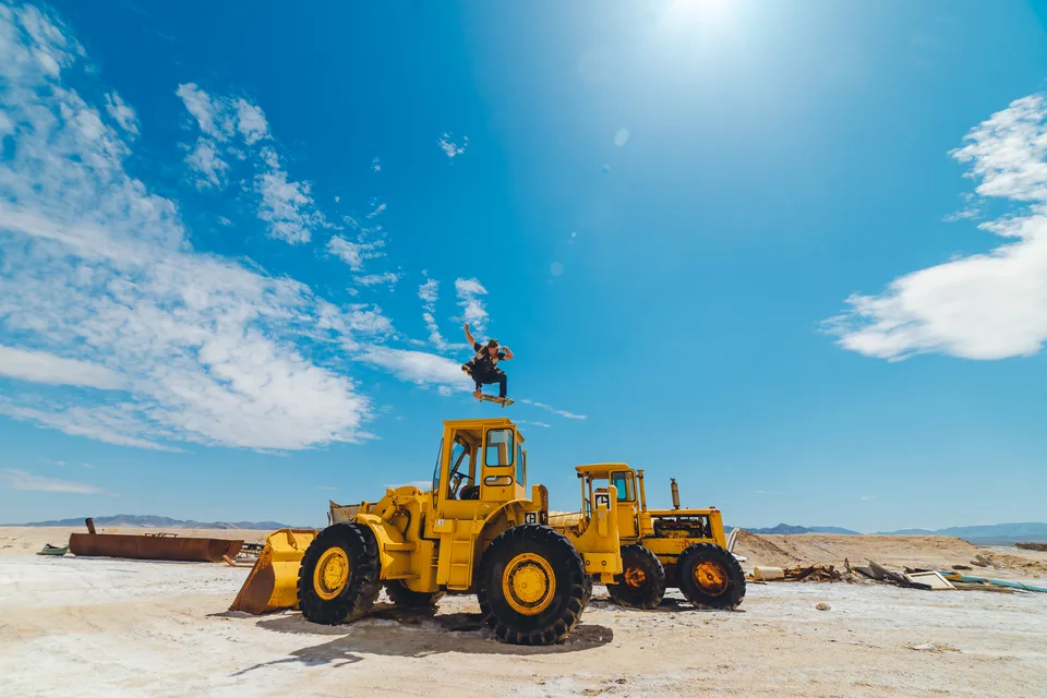 A skateboarder mid-jump above abandoned heavy equipment near Amboy, Mojave Desert, along Route 66, wide