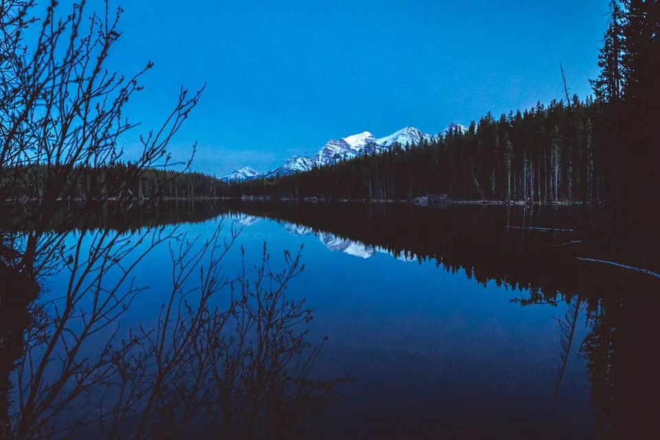 A mountain lake reflecting snow-capped peaks at blue hour, Banff, Alberta