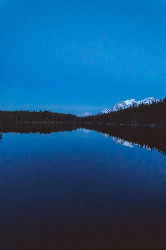 A mountain lake reflecting snow-capped peaks at blue hour, vertical, Banff, Alberta
