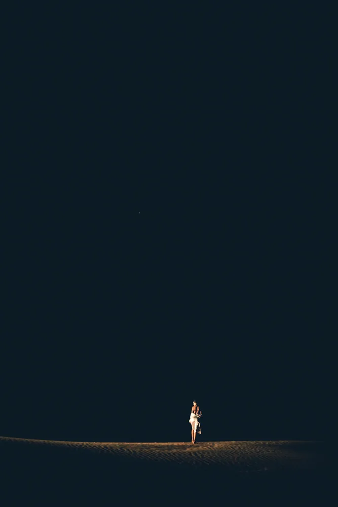 A figure lit dramatically on a dark dune at dusk, Glamis