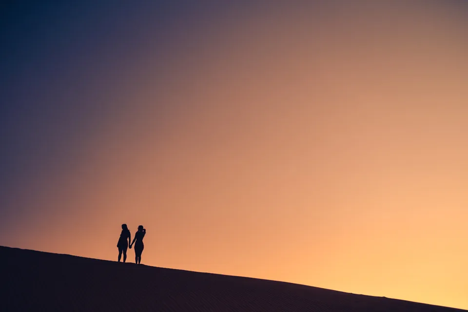 Two figures holding hands on a dune ridge at sunset, Glamis