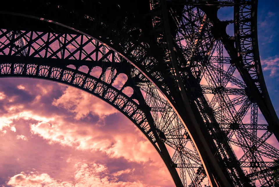 The underside of the Eiffel Tower's iron arch against a pink sunset sky, Paris