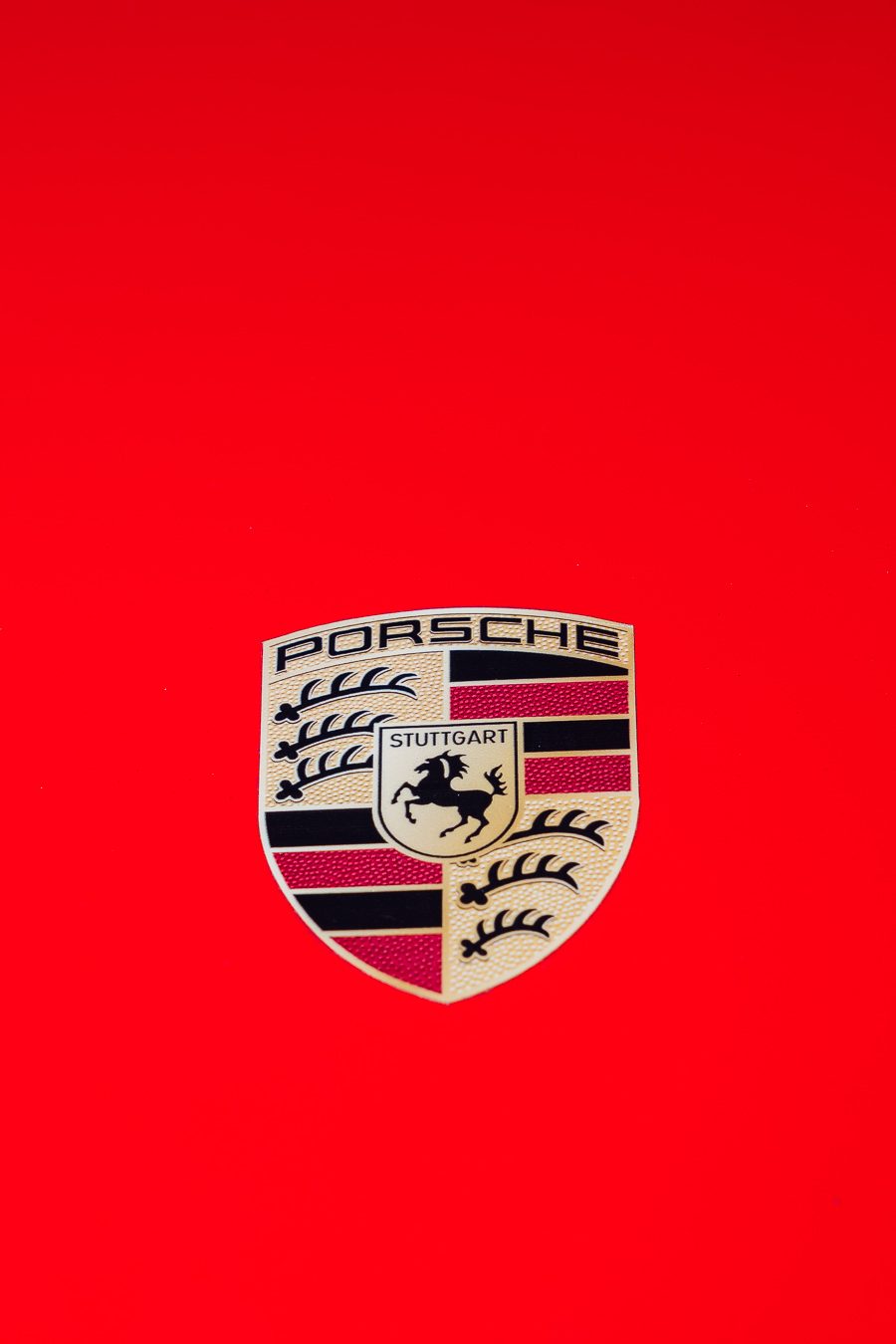 Porsche Stuttgart crest badge centered on Guards Red hood — minimalist automotive detail photography Newport Beach