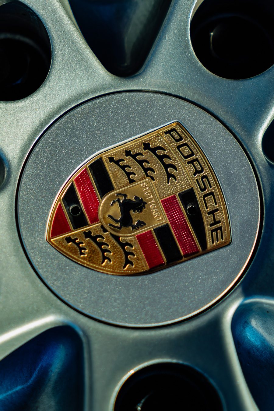 Porsche crest wheel center cap detail on silver alloy center-lock wheel, bokeh background