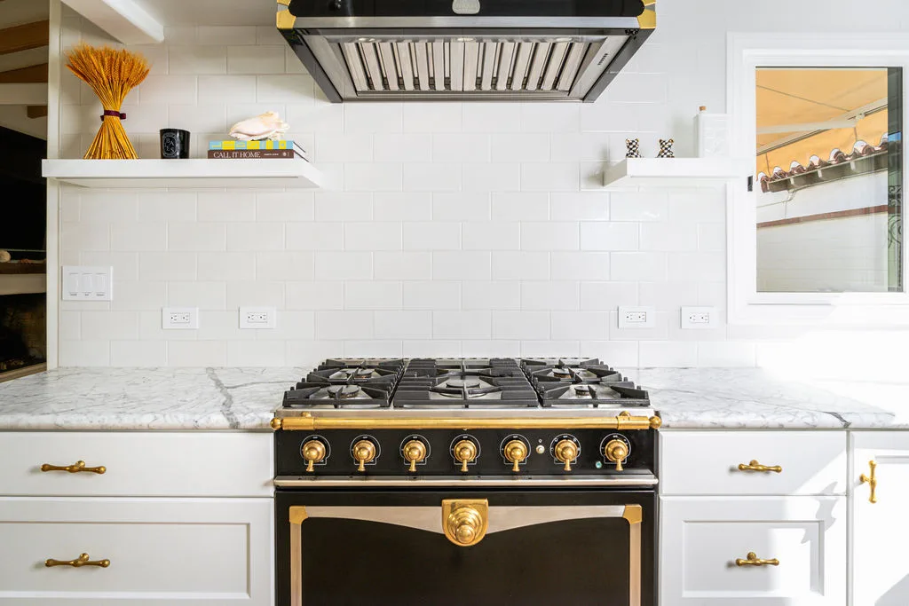 La Cornue cooktop with brass trim beneath floating shelves in a Newport Beach kitchen